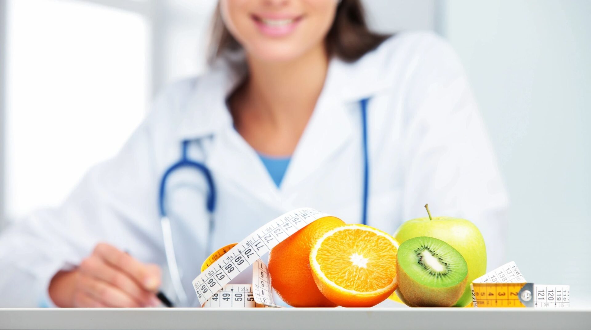 A doctor sitting at the table with fruits and an apple.