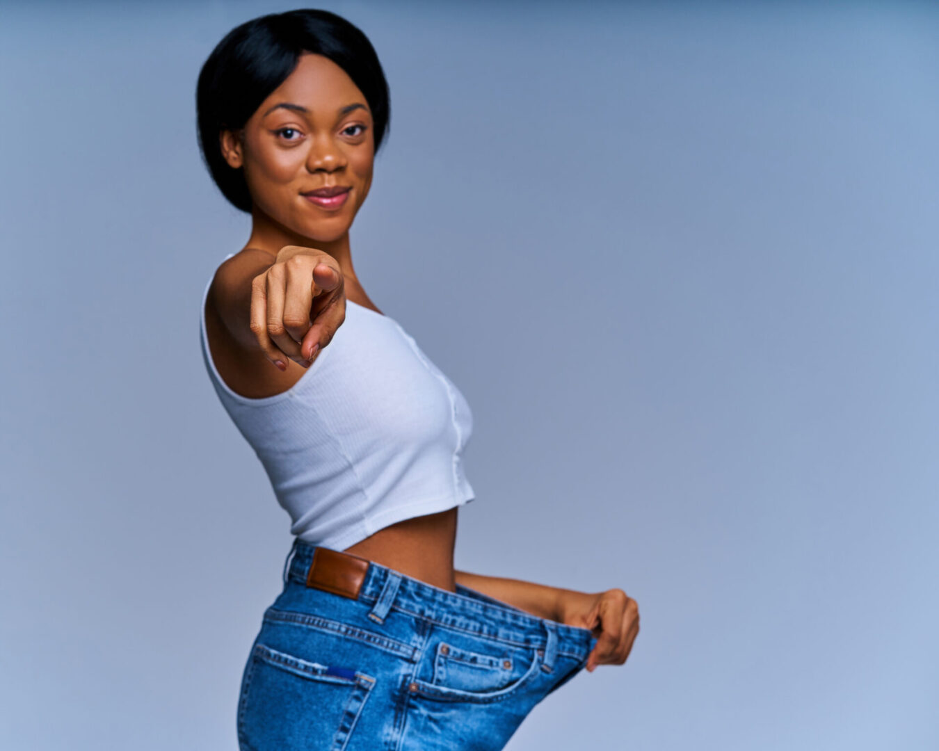 A woman in jeans is pointing to her waist.