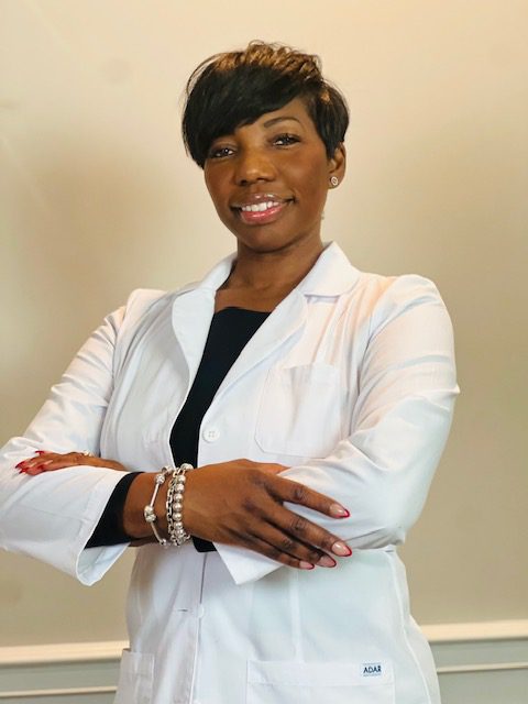 A woman in white jacket standing with her arms crossed.